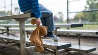 Young boy sitting by himself on bleachers and holding teddy bear.