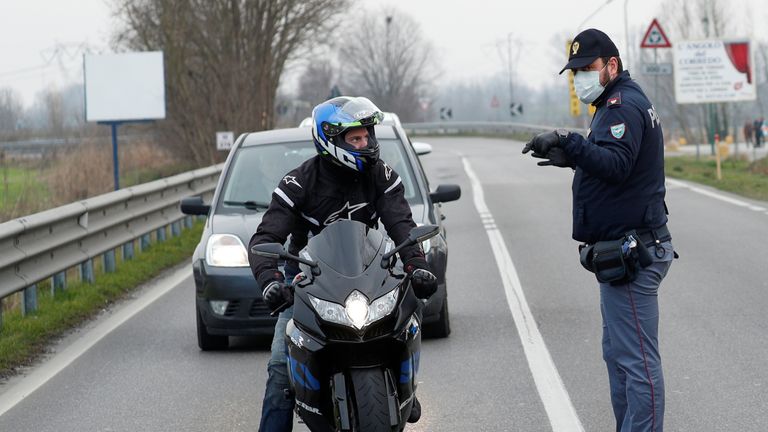 Policemen wearing face masks warn drivers on the road between Codogno and Casalpusterlengo, which has been closed by the Italian government due to a coronavirus outbreak in northern Italy, February 23, 2020. REUTERS/Guglielmo Mangiapane.