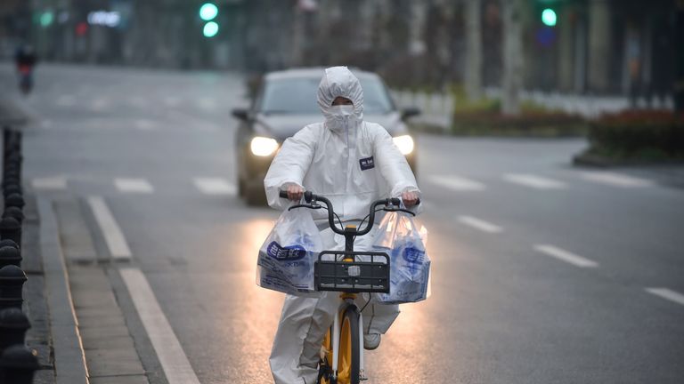 This photo taken on February 27, 2020 shows a resident wearing a protective suit riding a bicycle in Wuhan in China&#39;s central Hubei province. - China reported 44 more deaths from the novel coronavirus epidemic on February 28 and 327 fresh cases, the lowest daily figure for new infections in more than a month. (Photo by STR / AFP) / China OUT (Photo by STR/AFP via Getty Images)
