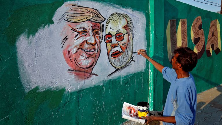 A man painting a picture of Donald Trump and Narendra Modi along the route the two men will take