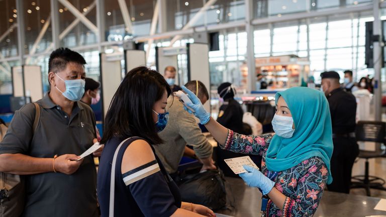 In this picture taken on February 14, 2020, a Malaysia Airlines hostess (R) wearing a protective face mask checks the temperature of Chinese passengers before they board a flight to Beijing at the Kuala Lumpur International Airport in Kuala Lumpur