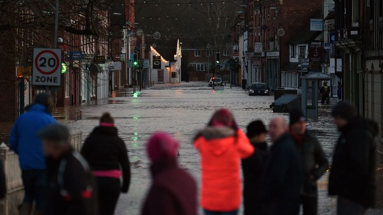 People look at flood water in a flooded street in Tenbury Wells, after the River Teme burst its banks in western England, on February 16, 2020, after Storm Dennis caused flooding across large swathes of Britain