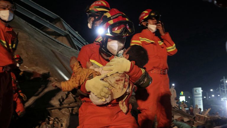 A worker wearing a face mask rescues a child at the site where a hotel being used for the coronavirus quarantine collapsed, in the southeast Chinese port city of Quanzhou, Fujian province, China