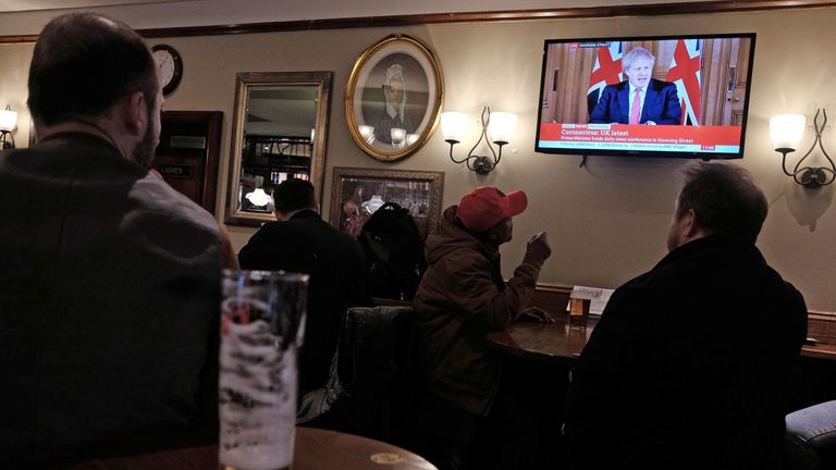 Drinkers watch a live broadcast of Prime Minister Boris Johnson as he announces he is closing pubs
