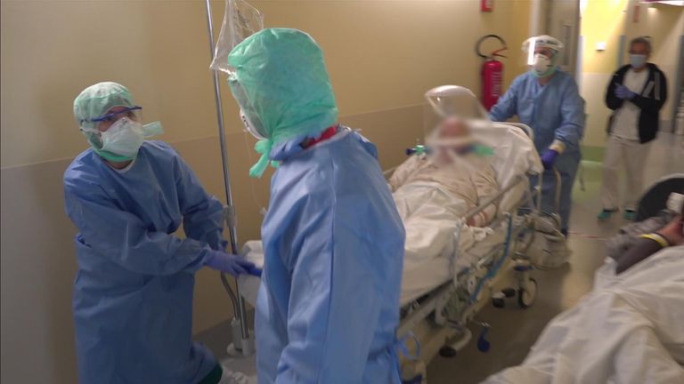 Hospital staff push a gurney carrying a man on a mobile respirator