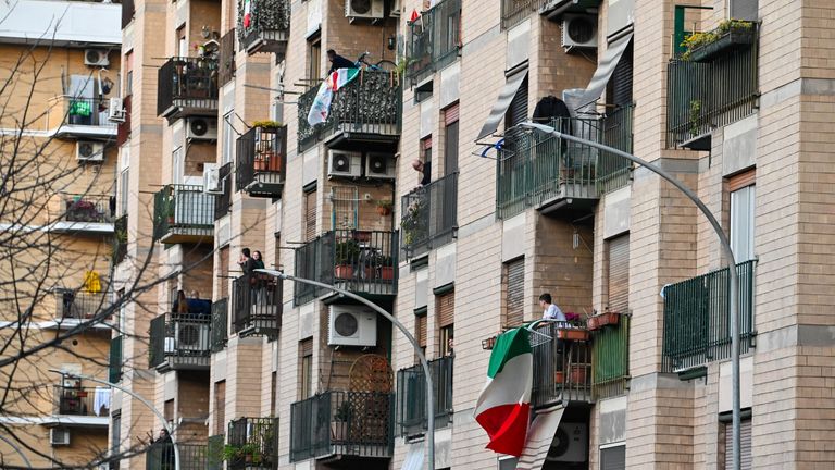 People wave and clap their hands next to a Italian flags, during a flash mob "Una canzone per l'Italia" (A song for Italy) at Magliana district in Rome on March 15, 2020. 