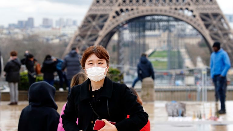 A tourist wears a protective mask as she poses in front of the Eiffel tower on March 2, 2020 in Paris, France