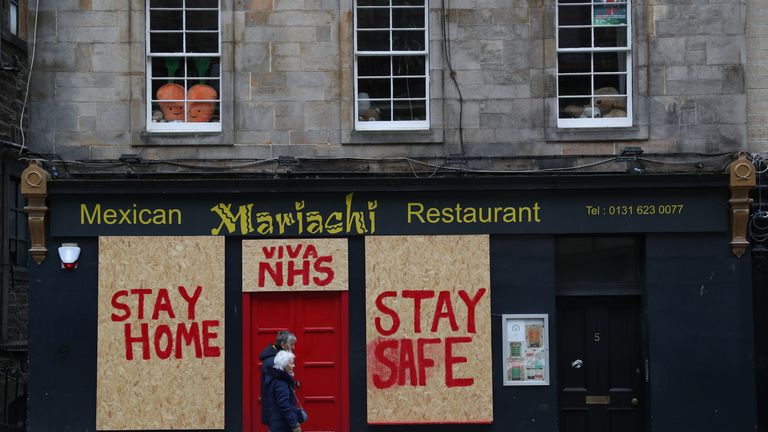 People pass a boarded up restaurant in Edinburgh which has been painted with an NHS supporting message as the UK continues in lockdown to help curb the spread of the coronavirus.