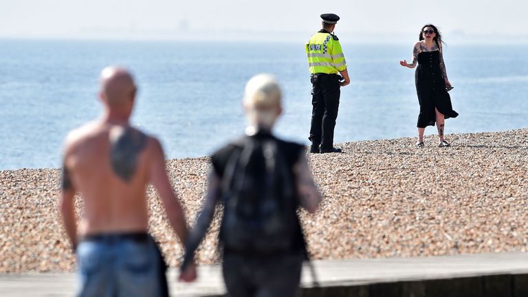 A police officer talks to a woman on the beach in Brighton, as the sunny bank holiday weather tests resolve