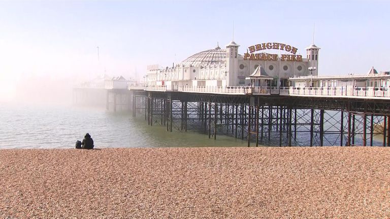 A solitary person sitting on beach at Brighton pier