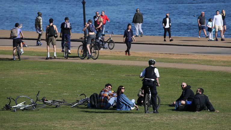 A police officer speaks to people relaxing by the Serpentine in Hyde Park, London