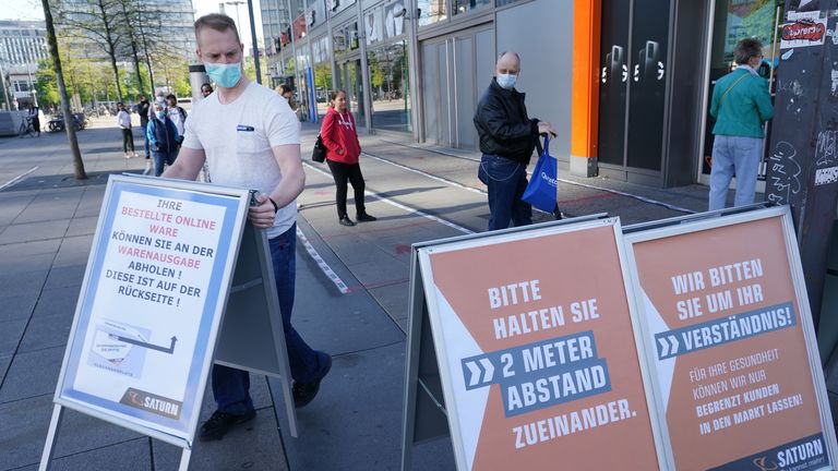 A shop assistant wearing a face mask places boards outside the Berlin store advising customers of social distancing