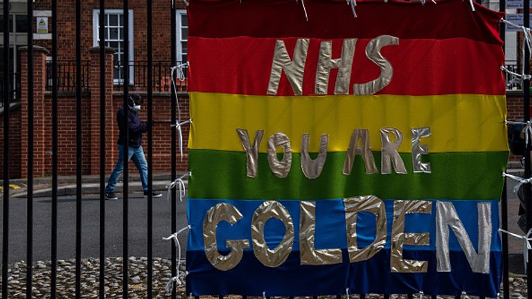 LONDON, ENGLAND  - APRIL 16: A man wearing a face mask walks behind a banner supporting Nation Health Service workers at Maudsley Hospital, opposition King..s College Hospital on April 16, 2020 in London, UK. The Coronavirus (COVID-19) pandemic has spread to many countries across the world, claiming over 130,000 lives and infecting over 2 million people. (Photo by Chris J Ratcliffe/Getty Images)