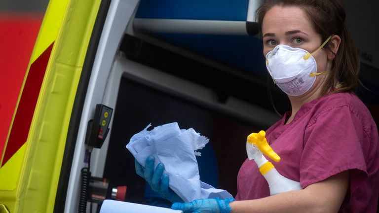 A London Ambulance worker wearing PPE cleans an ambulance