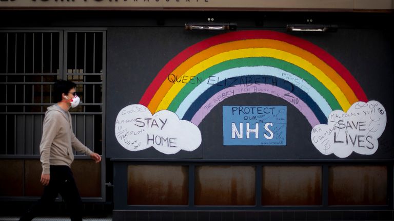 A man wearing a face mask walks past a rainbow graffiti in support of the NHS in Soho, central London, as the UK continues in lockdown to help curb the spread of the coronavirus.