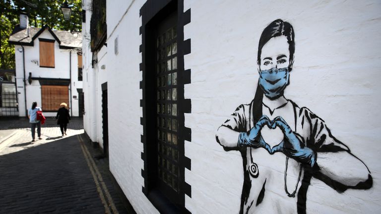 People walk past a piece of art by the artist, known as the Rebel Bear after it appeared on a wall on Ashton Lane in Glasgow. The new addition to Glasgow's street art is capturing the global Coronavirus crisis. The piece features a nurse wearing a mask and forming a love heart with her hands as the UK continues in lockdown to help curb the spread of the coronavirus.