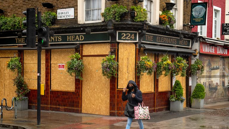 A woman walks past a boarded up pub in north London, as the UK continues in lockdown to help curb the spread of the coronavirus.