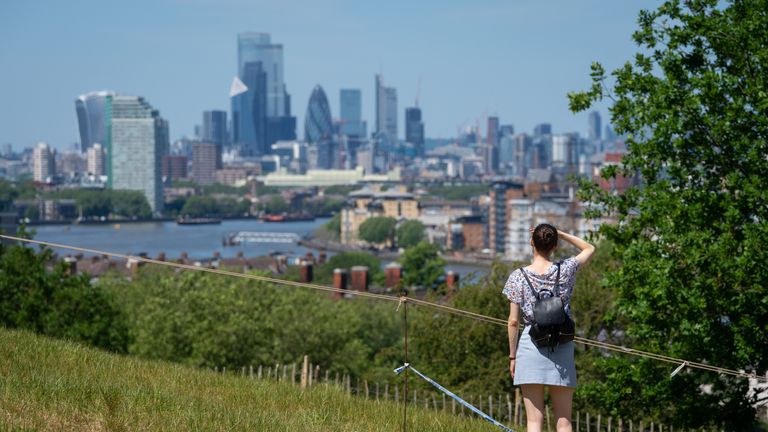 A woman looks out at the view of the London skyline as people enjoy the hot weather in Greenwich Park, London, flocking to parks and beaches with lockdown measures eased.