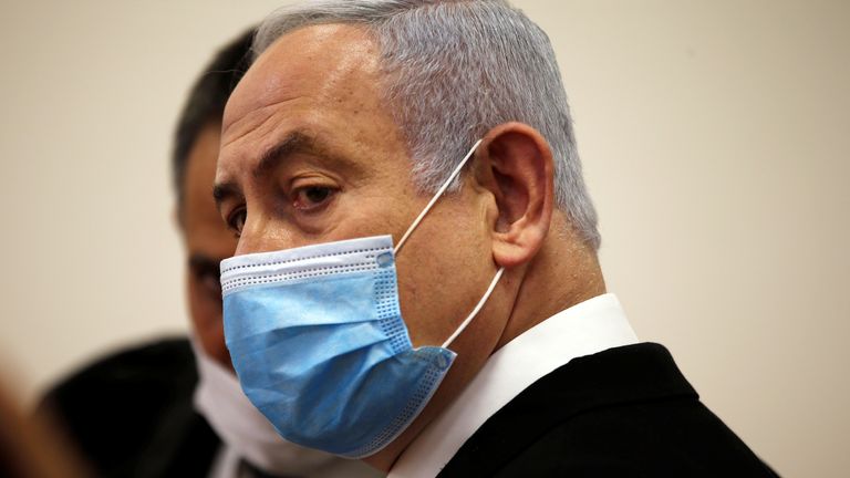 Israeli Prime Minister Benjamin Netanyahu, wearing a face mask, looks on while standing inside the court room as his corruption trial opens at the Jerusalem District Court