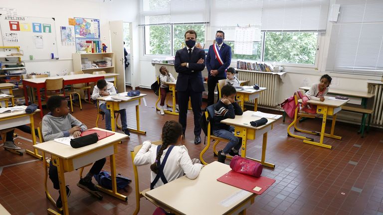French President Emmanuel Macron and Mayor of Poissy Karl Olive (back) wearing protective masks meet pupils as they visit the Pierre Ronsard elementary school in Poissy, west of Paris, on May 5, 2020 on the 50th day of a strict lockdown in France, in place to attempt to stop the spread of the new coronavirus (COVID-19). - French President visits a primary school as the virus lockdown is set to ease with partial lifting of restrictions such as the opening of primaries school. (Photo by Ian LANGSD