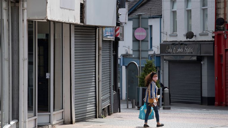 A woman wears a face mask and surgical gloves while carrying a bag and walking passed closed small businesses on High Street 