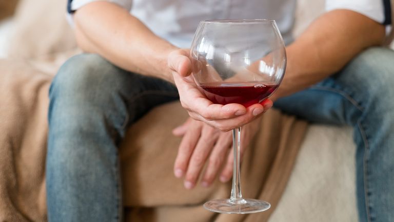 Problem, depression. Alcohol abuse. Man sitting with half empty red wine glass. Cropped shot. Home solitude.