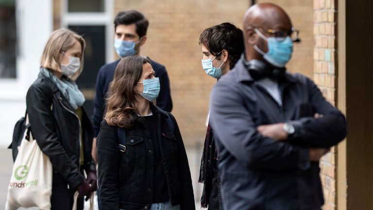 Members of the public in face masks queue 2 meters apart outside a shop in East London