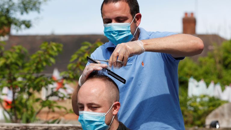 Hairdresser Pavlos cuts a mans hair in his garden as they both wear masks after his shop was shut due to government guidelines, following the outbreak of the coronavirus disease (COVID-19), Edmonton, Britain May 8, 2020