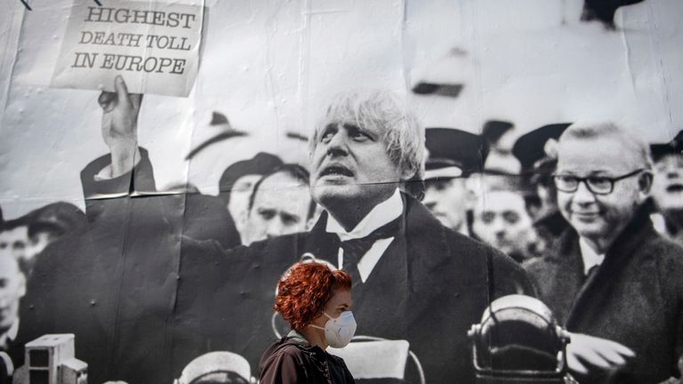 A woman in a mask walks past a satirical poster depicting Boris Johnson as former British prime minister Neville Chamberlain delivering his “Peace for Our Time” speech 