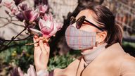 Woman wears reusable mask outdoors during coronavirus covid-19 pandemic. Girl smells magnolia spring flowers. Stay safe, positive. Spring fashion (Woman wears reusable mask outdoors during coronavirus covid-19 pandemic. Girl smells magnolia spring flo