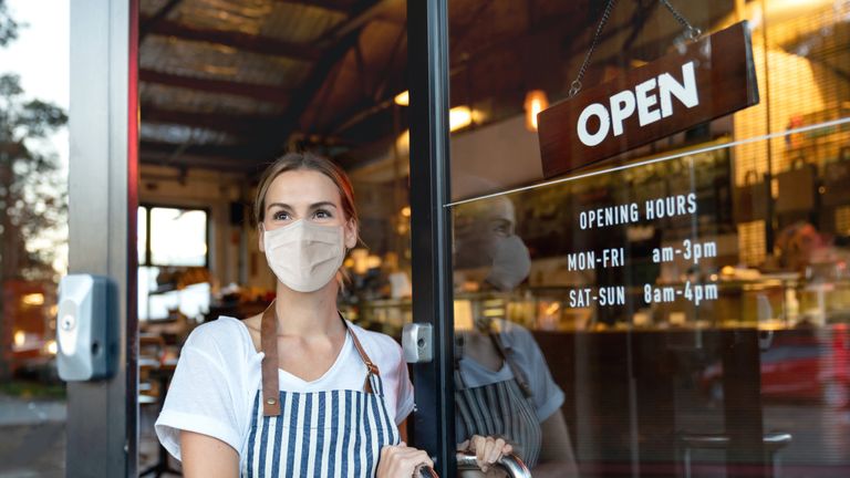 Happy business owner opening the door at a cafe wearing a facemask to avoid the spread of coronavirus â&#128;&#147; reopening after COVID-19 concepts