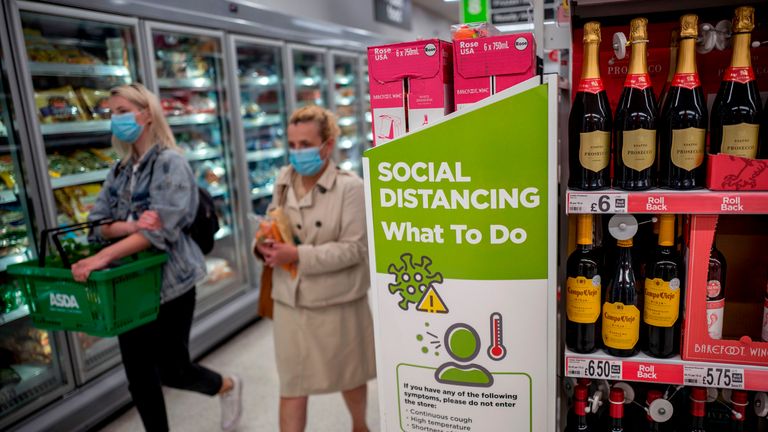 Shoppers wearing PPE (personal protective equipment), of a face mask or covering as a precautionary measure against spreading COVID-19,, walk past a banner advising customers to maintain the British government's current social distancing guidelines and stay two metres (2M) apart, inside an Asda supermarket store in Walthamstow, east London on June 22, 2020. - Britain's current social distancing guidelines set the distance between each person at two metres to avoid the risk of contamination to coronavirus. There is pressure on the government to reduce this distance in order to give a boost to bars, restaurants and hotels, which are scheduled to reopen next month. (Photo by Tolga AKMEN / AFP) (Photo by TOLGA AKMEN/AFP via Getty Images)