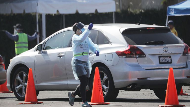 A worker signals to motorists at a drive-in COVID-19 testing site in Los Angeles, California, which has seen a surge in cases