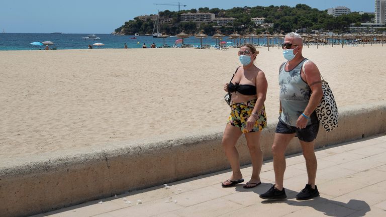 Mask-wearing holidaymakers walk along a beachfront  Balearic island of Majorca