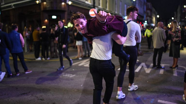 A man is seen being carried on his friend's shoulders in Soho