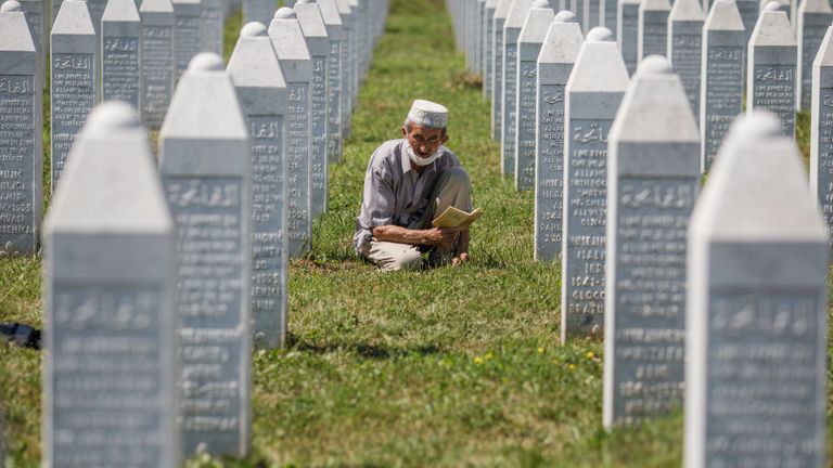 A Bosnian Muslim man reads a religious book between graves