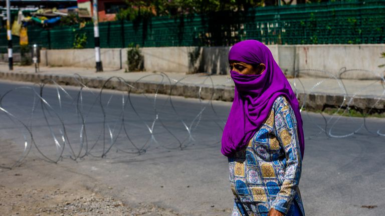 SRINAGAR, KASHMIR - INDIA - AUGUST 05: A Kashmiri Muslim woman walks in front of a concertina razor wire of Indian government forces closing a road in the deserted city center during a curfew like restrictions, a year after India revoked the special status of Jammu and Kashmir, in the city center  on August 05, 2020  in Srinagar, the summer capital of Indian administered Kashmir, India. Indian police and paramilitary personnel were deployed in strength as authorities imposed curfew-like restrictions in summer capital city Srinagar  on the first anniversary of the Indian government stripping the Himalayan region, contested by both India and Pakistan since 1947, of its autonomy and downgrading its status from a state to a union  territory in a stealth move last year. The region is already reeling under a lockdown imposed by authorities to curb the spread of coronavirus. (Photo by Yawar Nazir/Getty Images)
