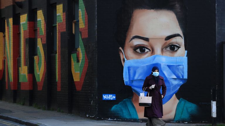 LONDON, ENGLAND - APRIL 21: A woman wearing a face mask walks past a piece of street art depicting an NHS worker on April 21, 2020 in the Shoreditch area of London, England. The British government has extended the lockdown restrictions first introduced on March 23 that are meant to slow the spread of COVID-19. (Photo by Andrew Redington/Getty Images)