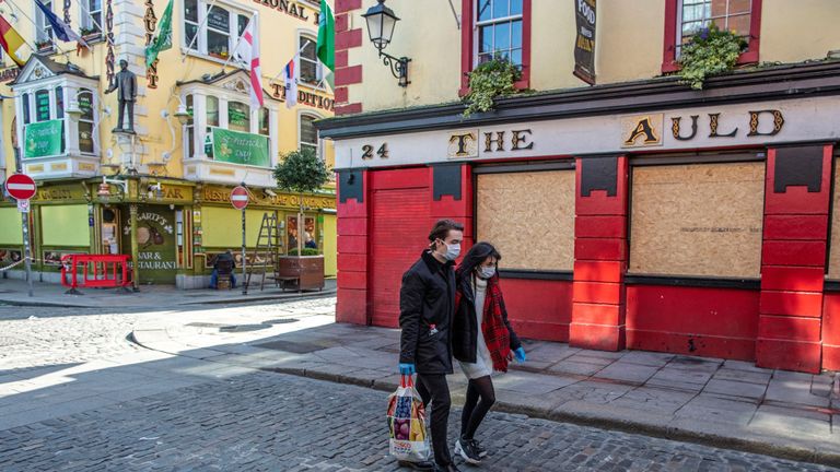 People wearing face mask as a precautionary measure against Covid-19, carry a shopping bag as the pass a boarded-up and temporarily closed pub in Dublin, on March 25, 2020, after Ireland introduced measures to help slow the spread of the novel coronavirus. - Ireland's prime minister Leo Varadkar on Tuesday announced that all non-essential businesses will shut from midnight  as part of the country's latest measures to tackle the coronavirus outbreak. "These are unprecedented actions to respond to an unprecedented emergency," he said, adding the measures would remain in place until at least April 19. (Photo by PAUL FAITH / AFP) (Photo by PAUL FAITH/AFP via Getty Images)