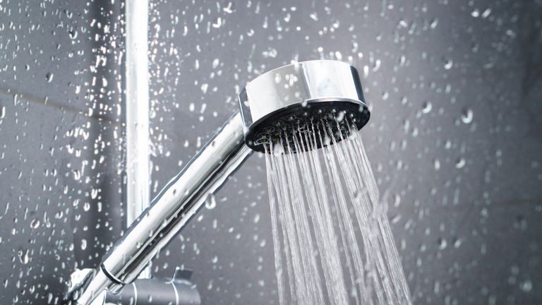 Fresh shower behind wet glass window with water drops splashing. Water running from shower head and faucet in modern bathroom.