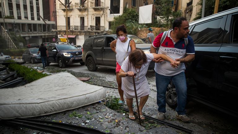 An elderly woman is helped while walking through debris 