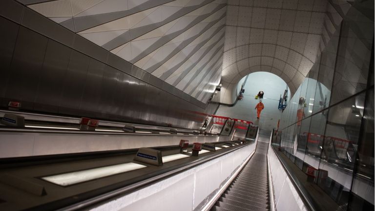 A member of the construction team works on the flooring at the base of an escalator 