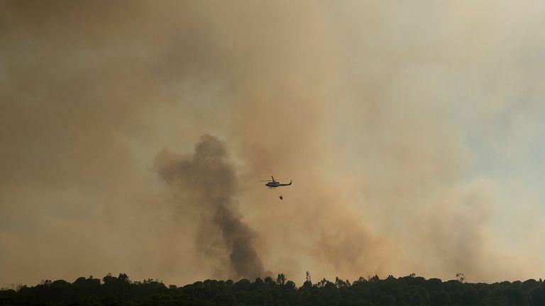 A helicopter drops water over a wildfire raging near El Buitron in Huelva, Spain