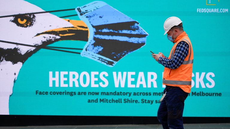 A key workers in Victoria walks past a sign encouraging people to wear masks