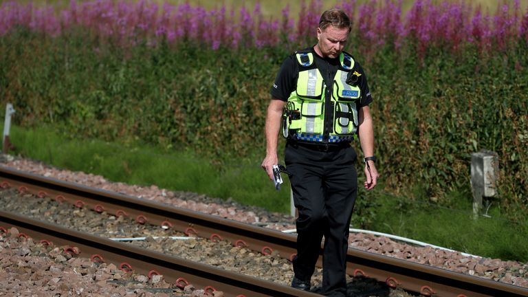 A police officer is seen walking along the track near to the scene where the train derailed 