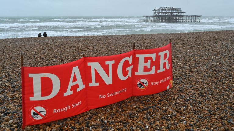 A couple walk on the beach near to a warning sign advising against swimming as a rough sea surrounds the derelict west pier in Brighton on the south coast of England on August 25, 2020. - Wind gusts of 70mph are expected as Storm Francis brings rain and high winds to the country. (Photo by Glyn KIRK / AFP) (Photo by GLYN KIRK/AFP via Getty Images)