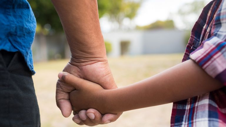 Cropped image of boy and grandfather holding hands while standing in yard