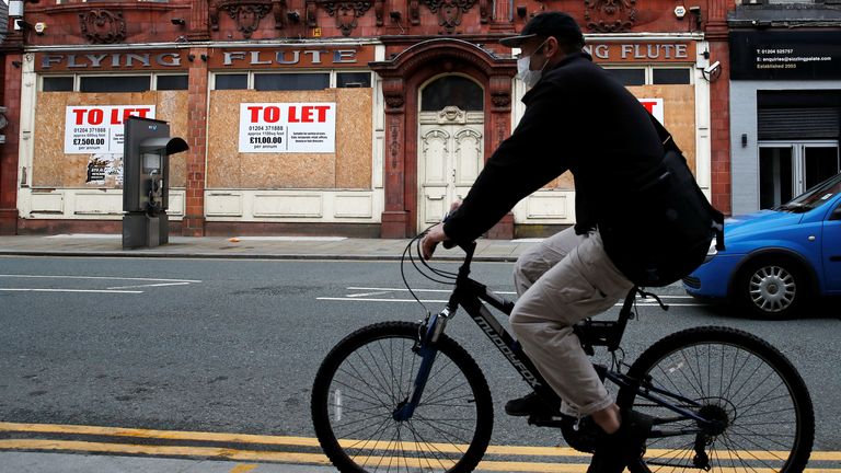 A mask-wearing cyclist is seen passing a closed shop in coronavirus-hit Bolton
