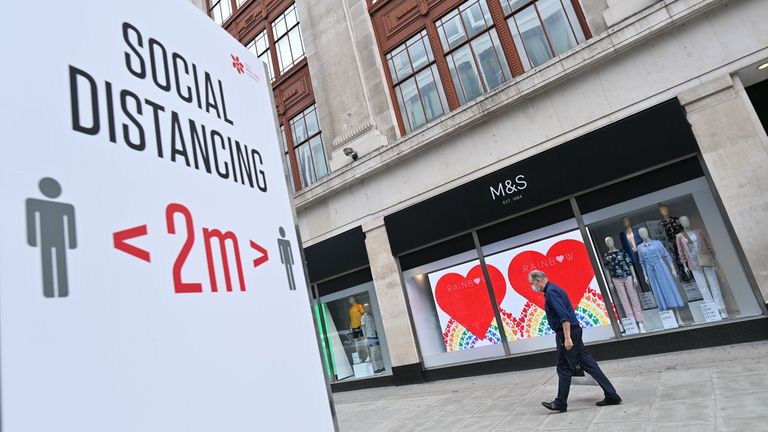 A shopper wearing a facemask as a precaution against the spread of the novel coronavirus walks past a store of the clothing and food retailer Marks and Spencer in central London on August 18, 2020 with social distancing advice displayed on the high street