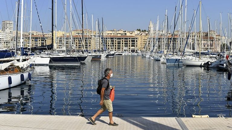 A man wearing a face mask walks on a pier on the Vieux-Port of Marseille